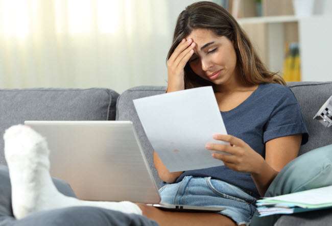 sad woman with leg cast looking at medical bill